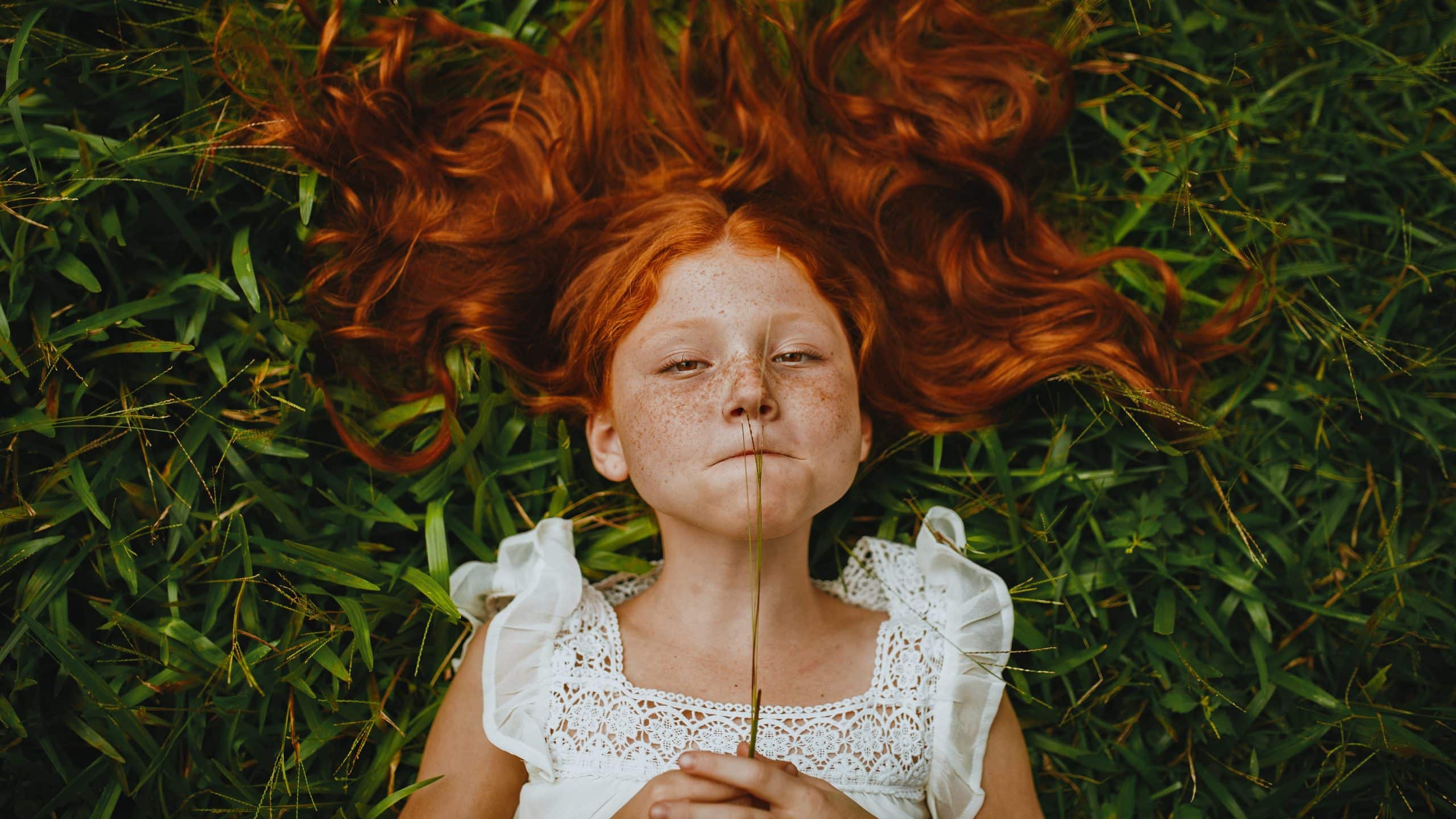 An image of a kid with long red hair lying on grass
